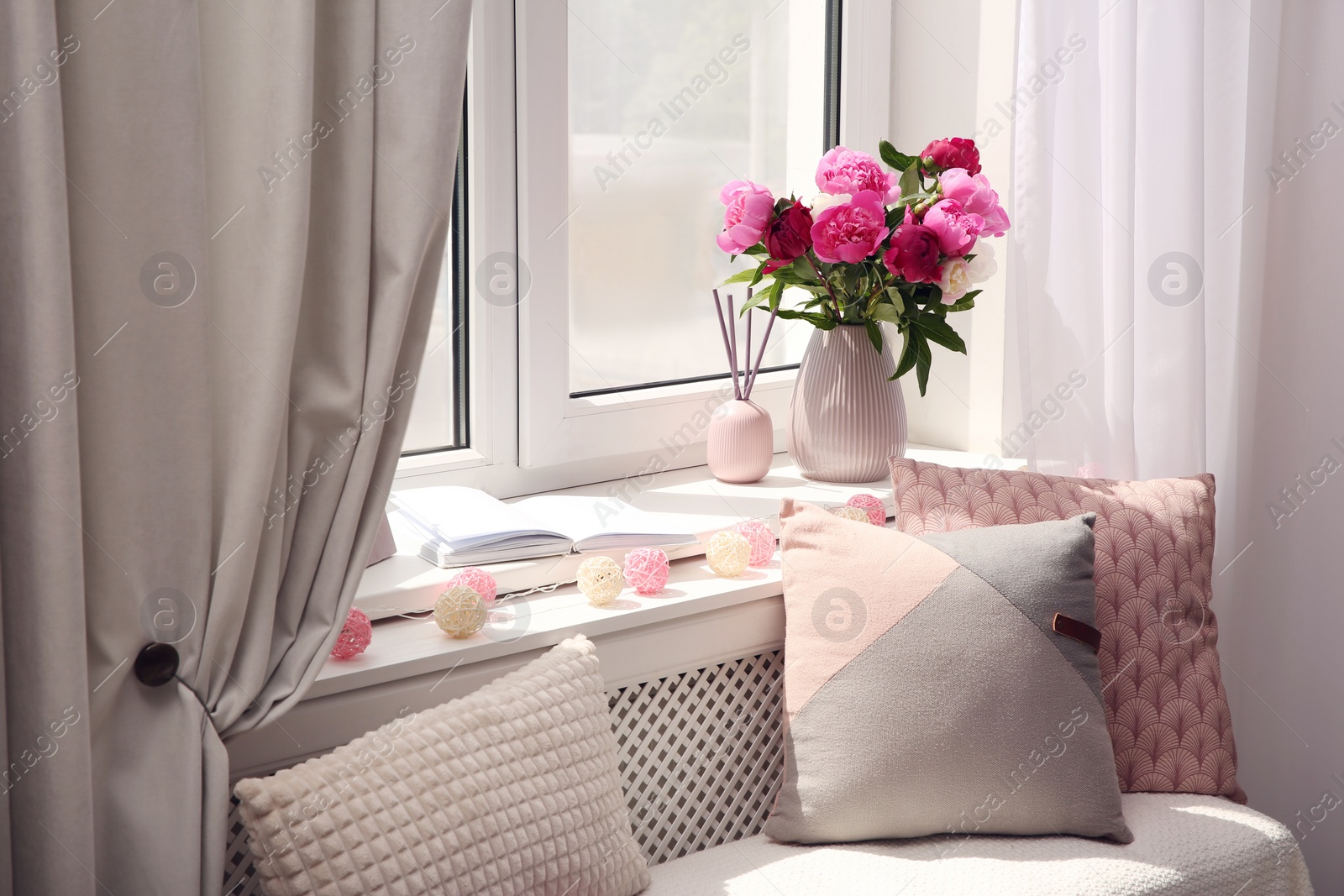 Photo of Comfortable place for rest with cushions and peony flowers near window indoors