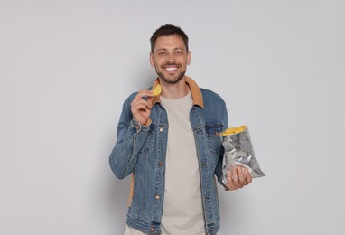 Handsome man with potato chips on light grey background