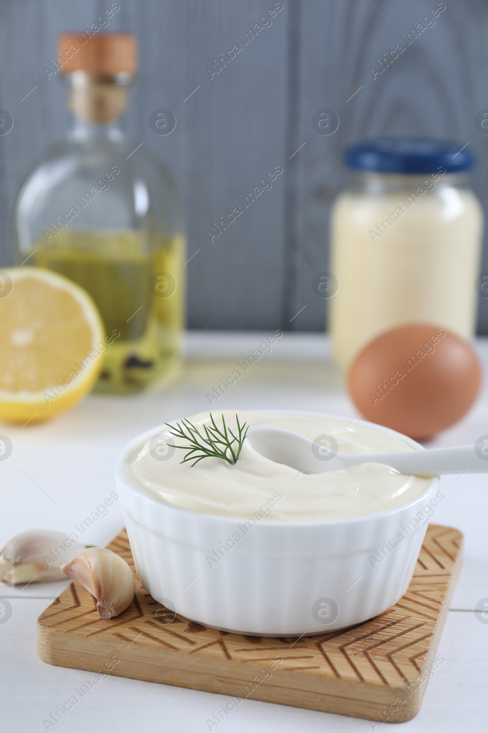 Photo of Fresh mayonnaise sauce in bowl and ingredients on white table