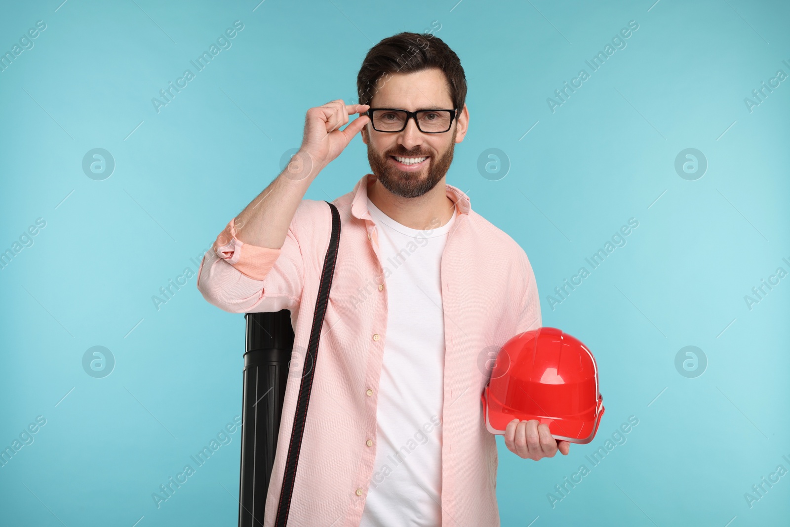 Photo of Architect with drawing tube and hard hat on light blue background