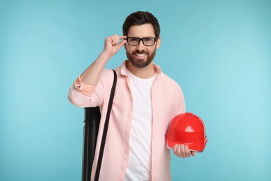 Photo of Architect with drawing tube and hard hat on light blue background