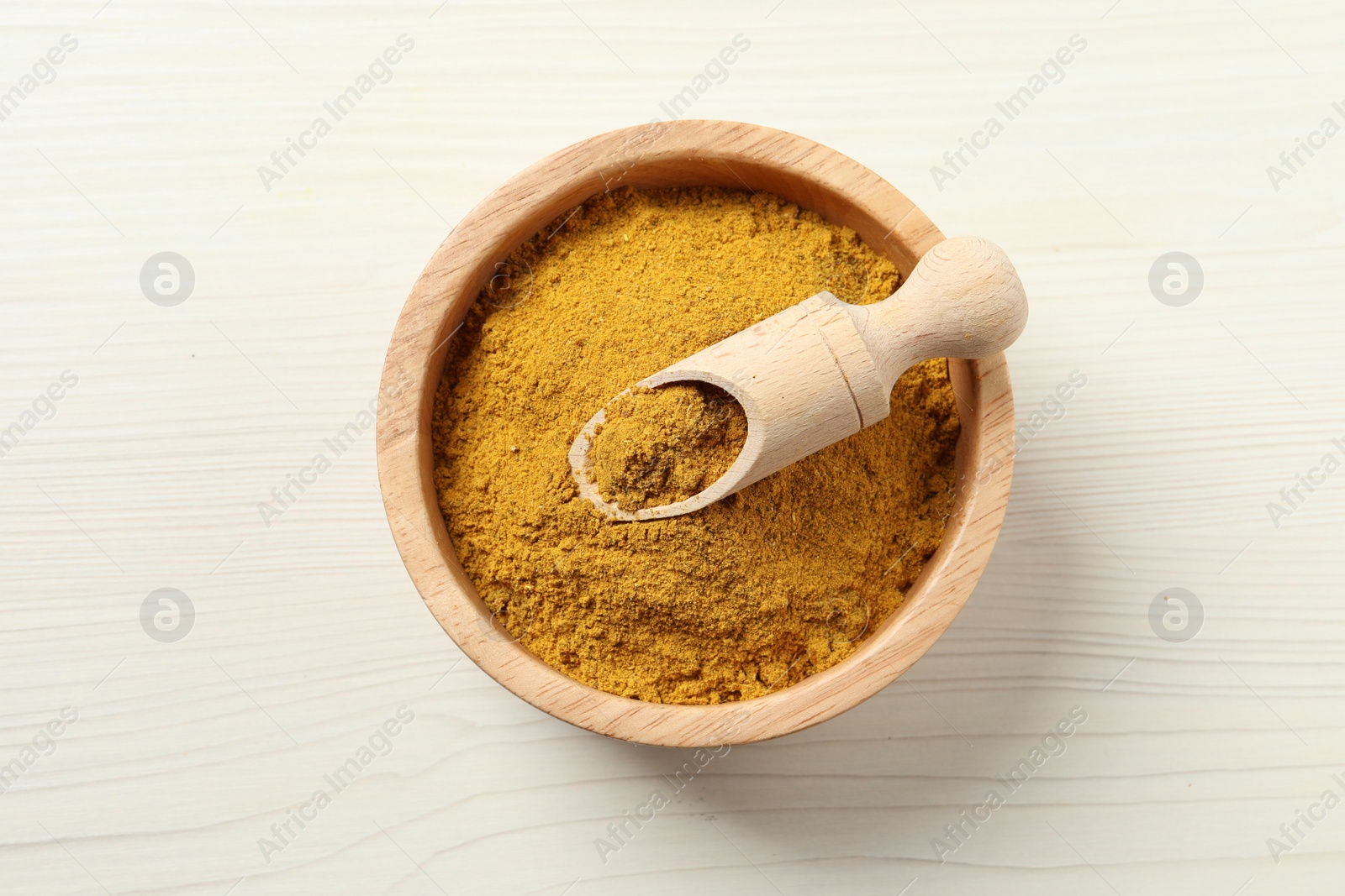 Photo of Dry curry powder in bowl and scoop on light wooden table, top view