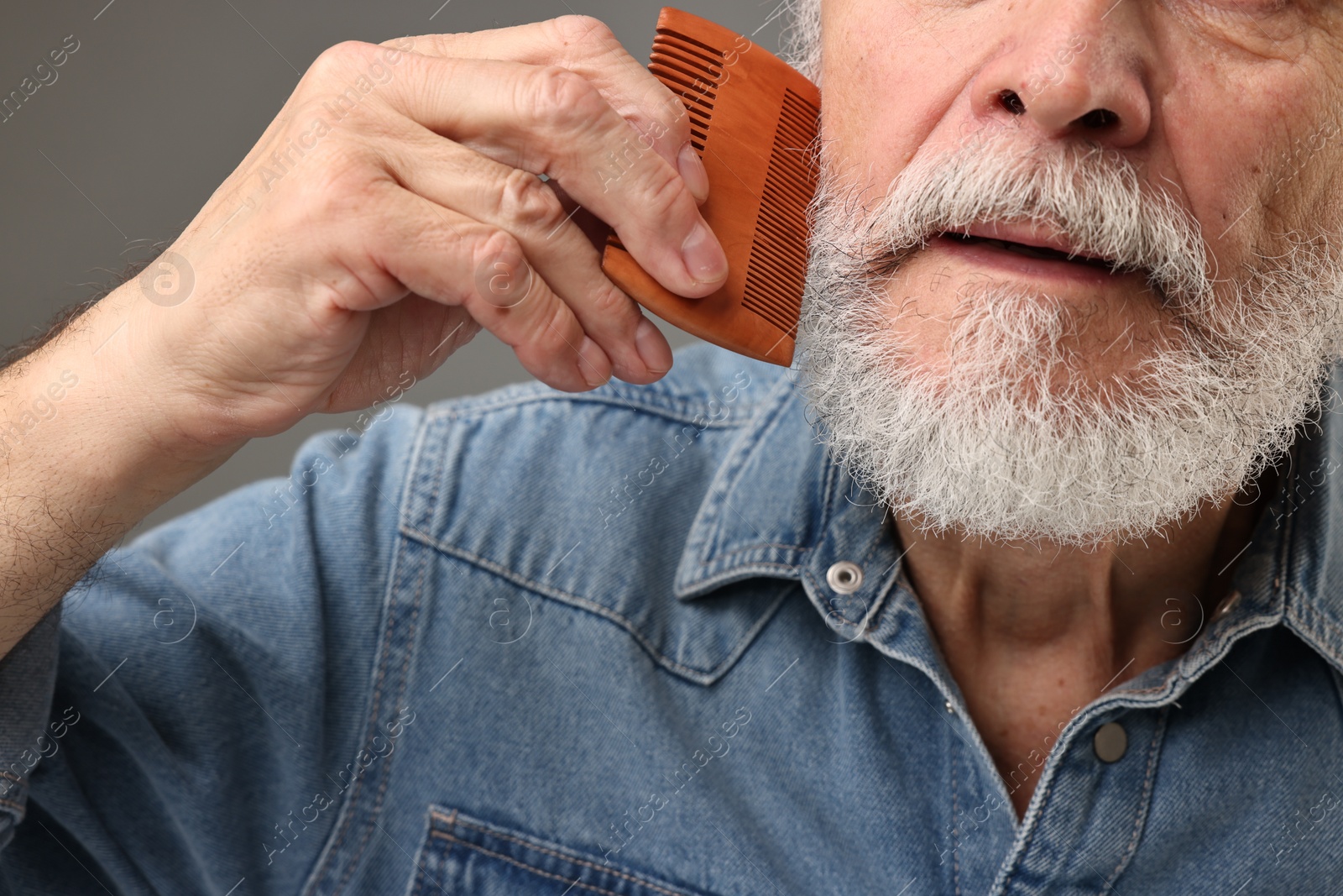 Photo of Man combing beard on grey background, closeup