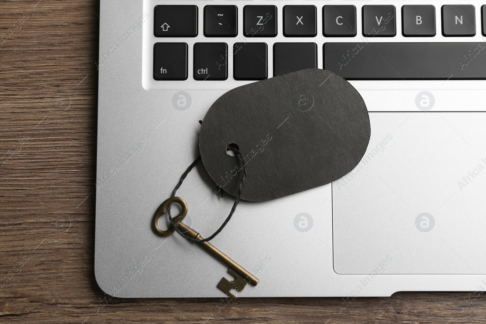 Photo of Vintage key with blank tag and laptop on wooden table, top view. Keyword concept