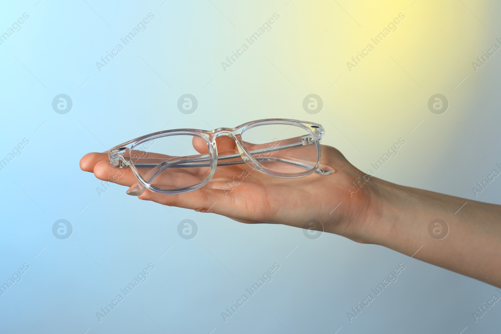 Photo of Woman holding glasses with transparent frame on color background, closeup