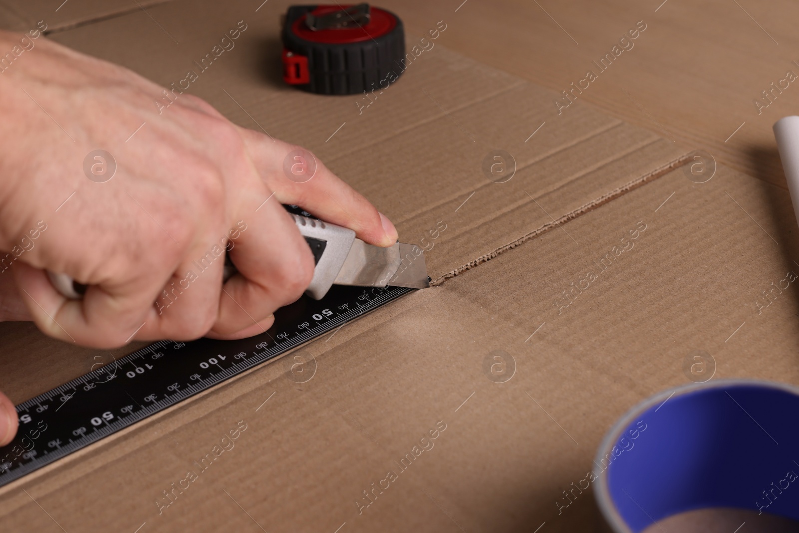 Photo of Man cutting cardboard with utility knife and ruler, closeup