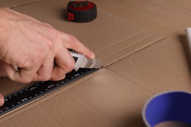 Man cutting cardboard with utility knife and ruler, closeup