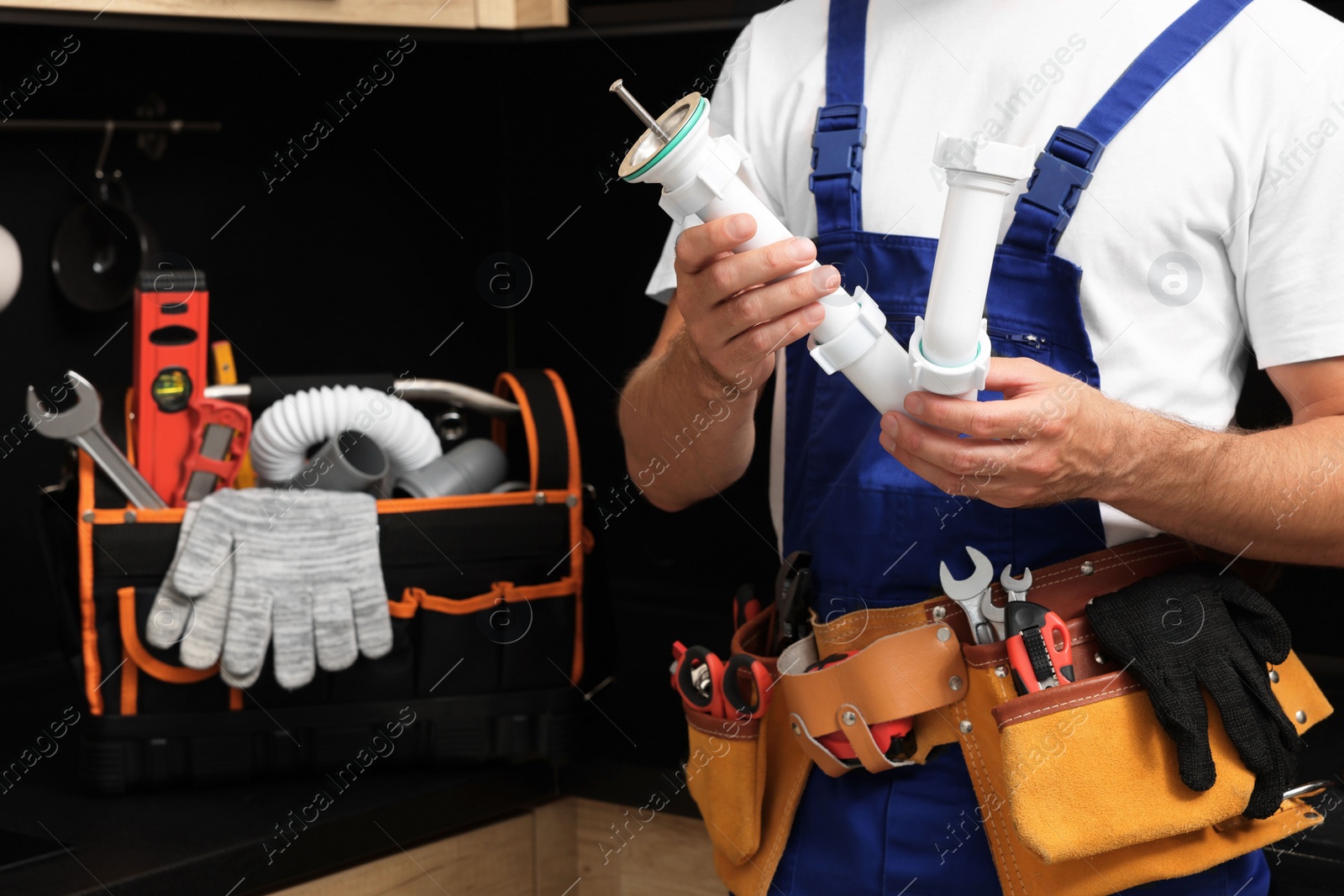 Photo of Professional plumber with corrugated pipe and tool belt indoors, closeup