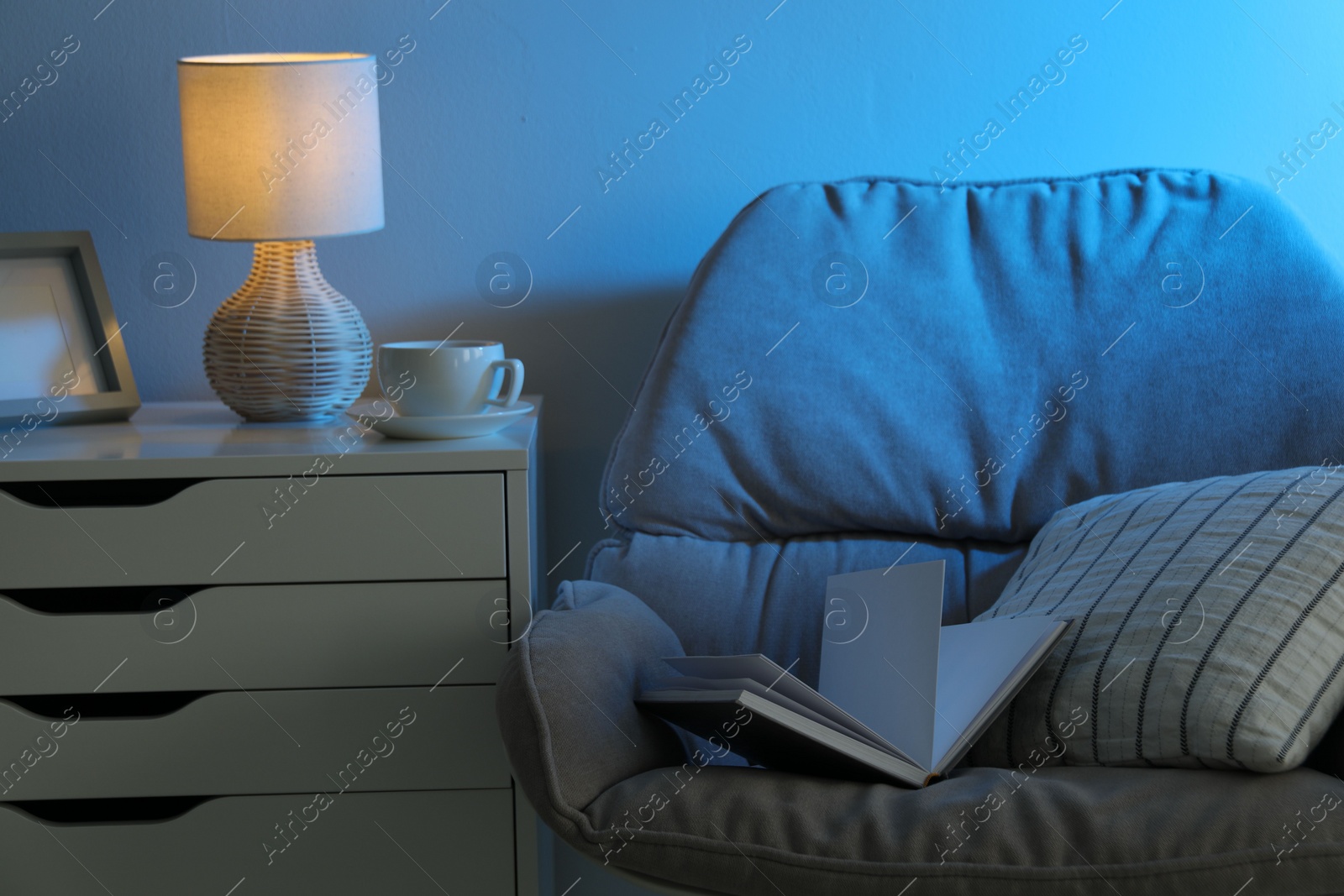 Photo of Comfortable armchair and white chest of drawers in room at night