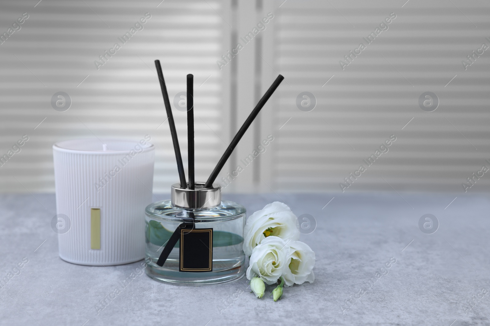 Photo of Reed diffuser, scented candle and eustoma flowers on gray marble table, space for text