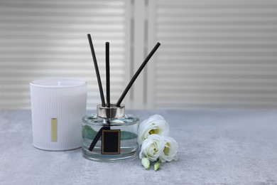 Reed diffuser, scented candle and eustoma flowers on gray marble table, space for text