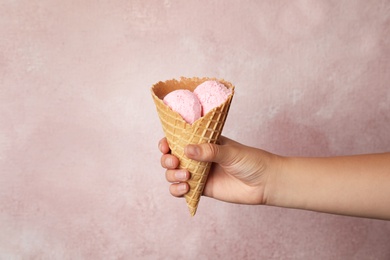 Photo of Woman holding delicious ice cream in wafer cone on pink background, closeup