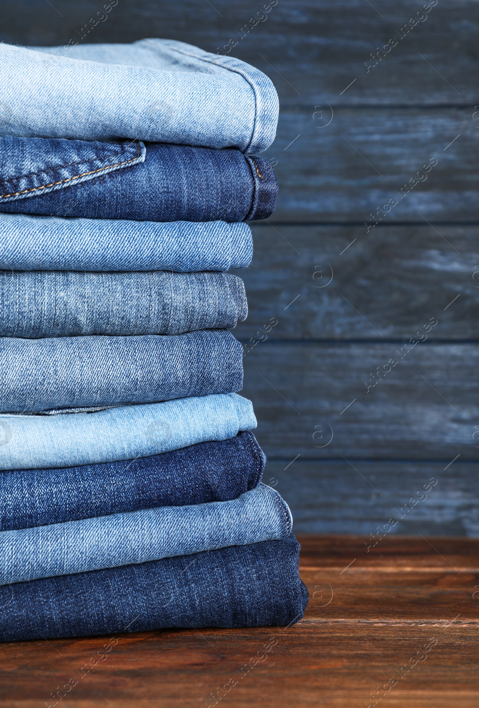 Photo of Stack of different jeans on wooden table. Space for text