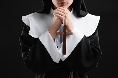 Photo of Nun with cross praying to God on black background, closeup