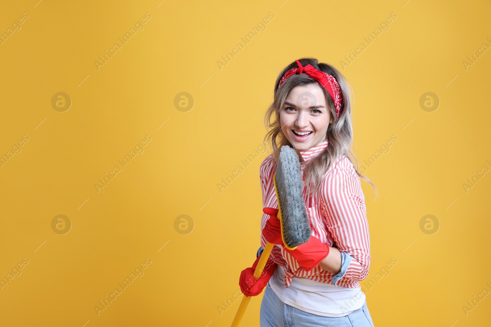 Photo of Beautiful young woman with floor brush singing on orange background. Space for text