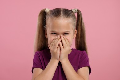 Photo of Embarrassed little girl covering her mouth with hands on pink background