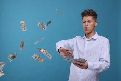 Photo of Handsome man throwing dollar banknotes on light blue background