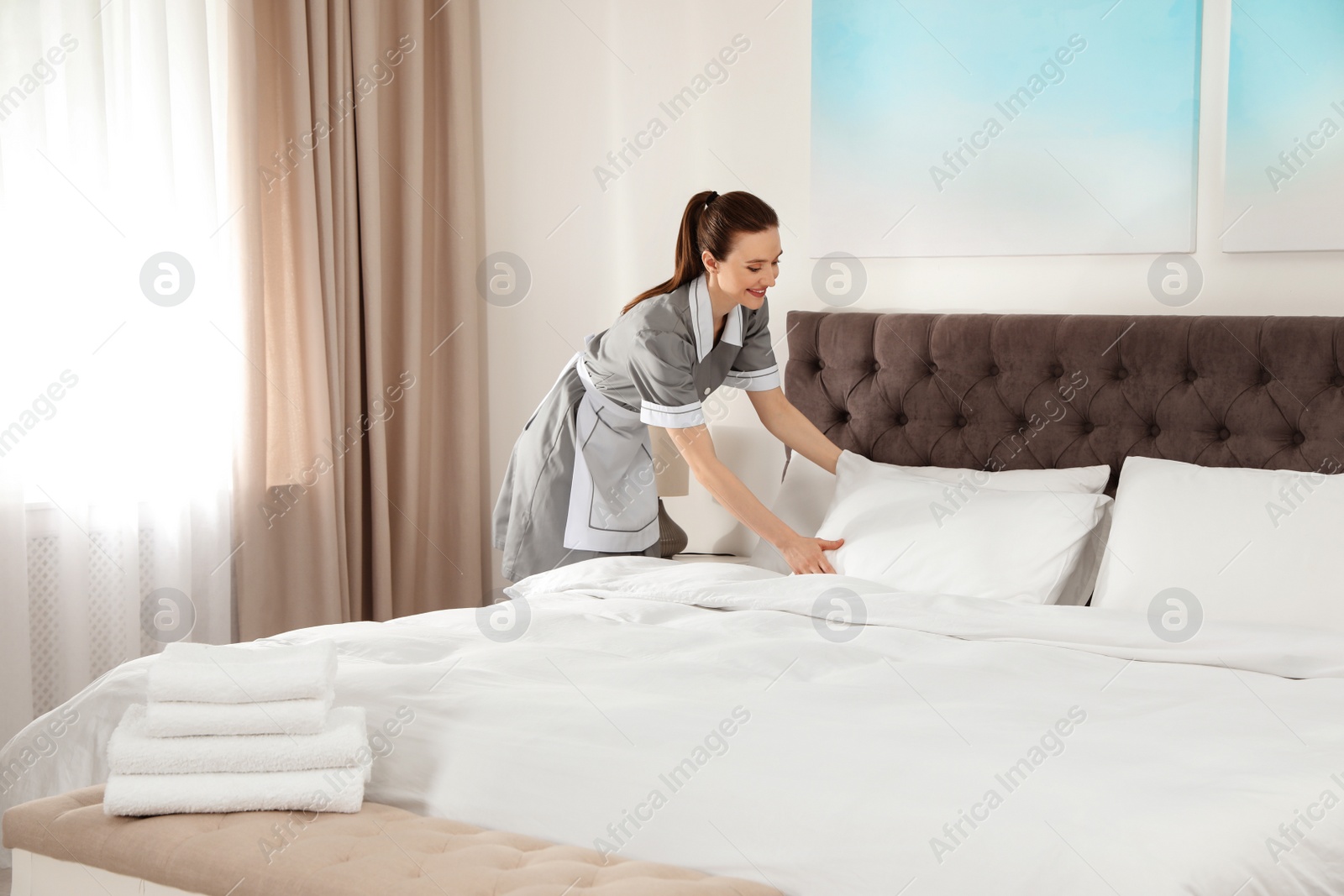 Photo of Young chambermaid making bed in hotel room. Space for text