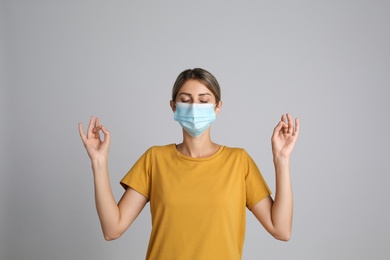 Photo of Woman in protective mask meditating on grey background. Dealing with stress caused by COVID‑19 pandemic