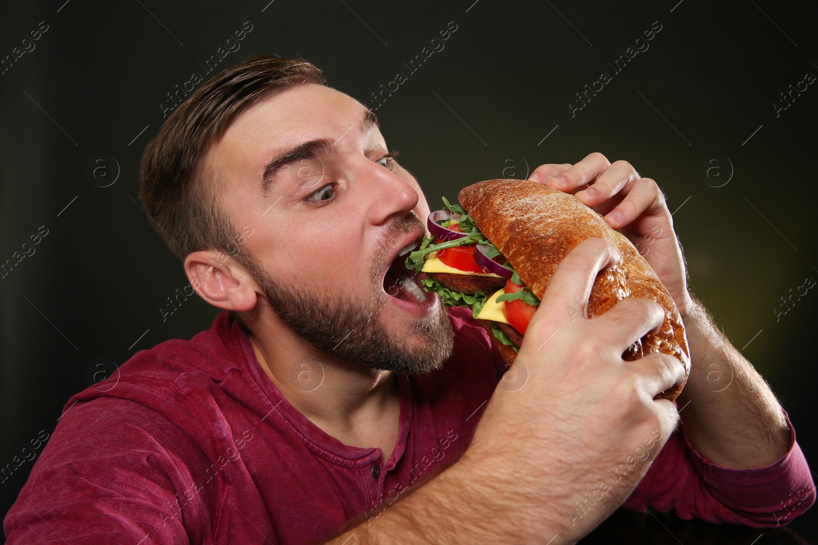 Photo of Young man eating tasty burger on color background