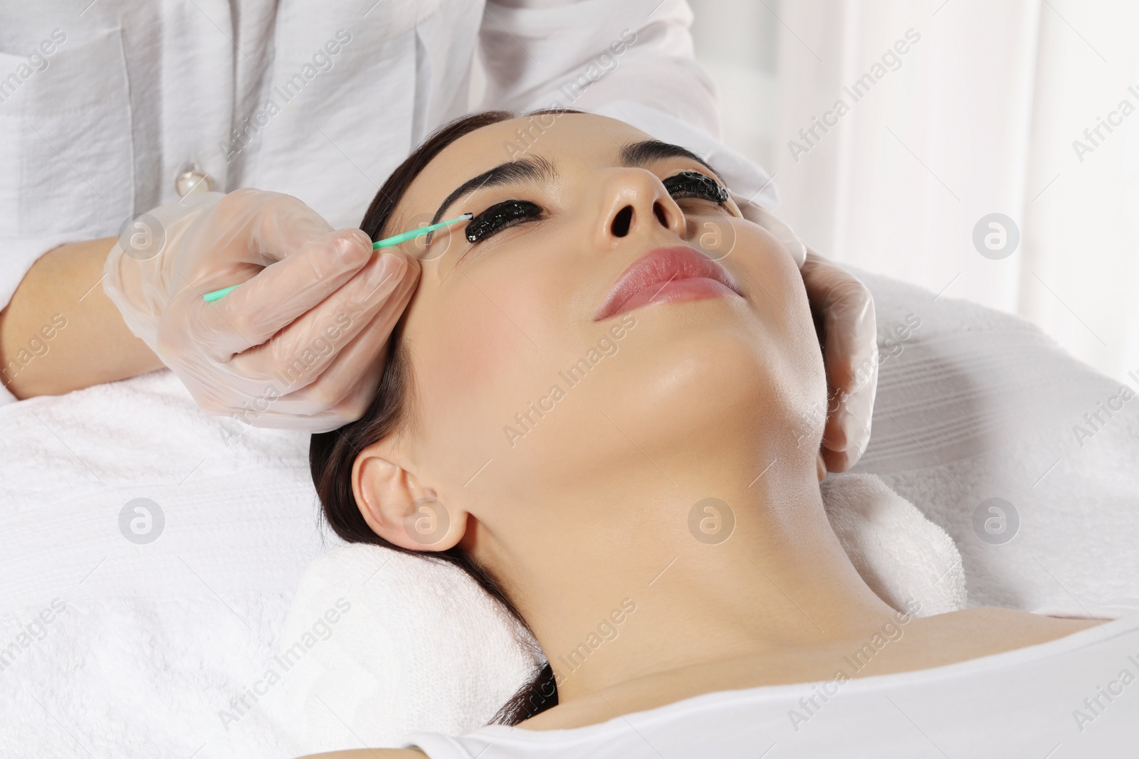 Photo of Young woman undergoing eyelash lamination and tinting in salon