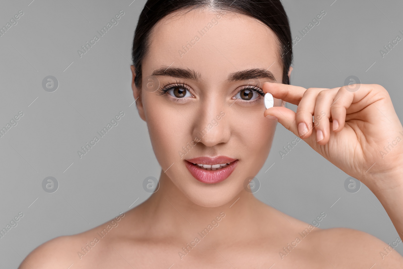 Photo of Beautiful young woman with vitamin pill on grey background