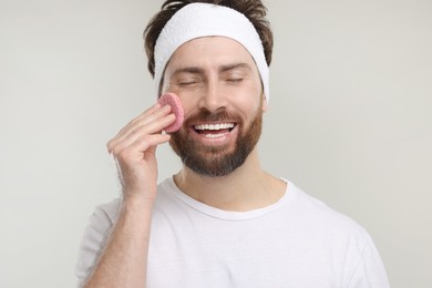 Photo of Man with headband washing his face using sponge on light grey background