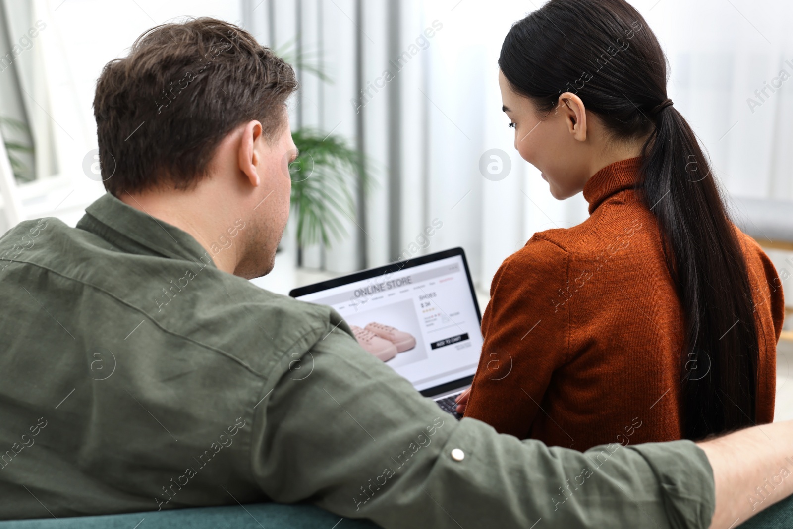 Photo of Couple with laptop shopping online indoors, back view