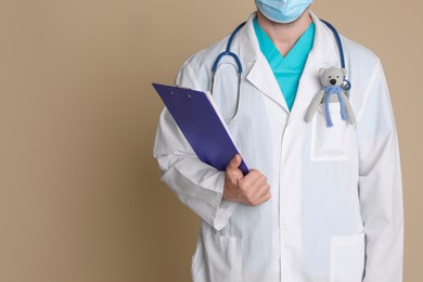 Pediatrician with toy bear and stethoscope on beige background, closeup. Space for text