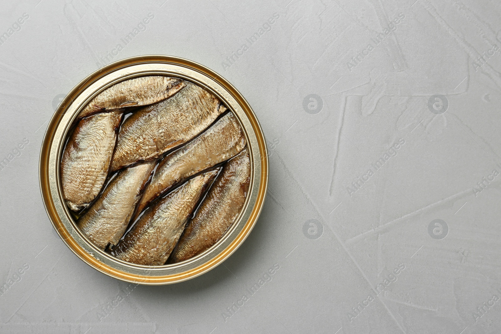 Photo of Open tin can of sprats on light grey table, top view. Space for text