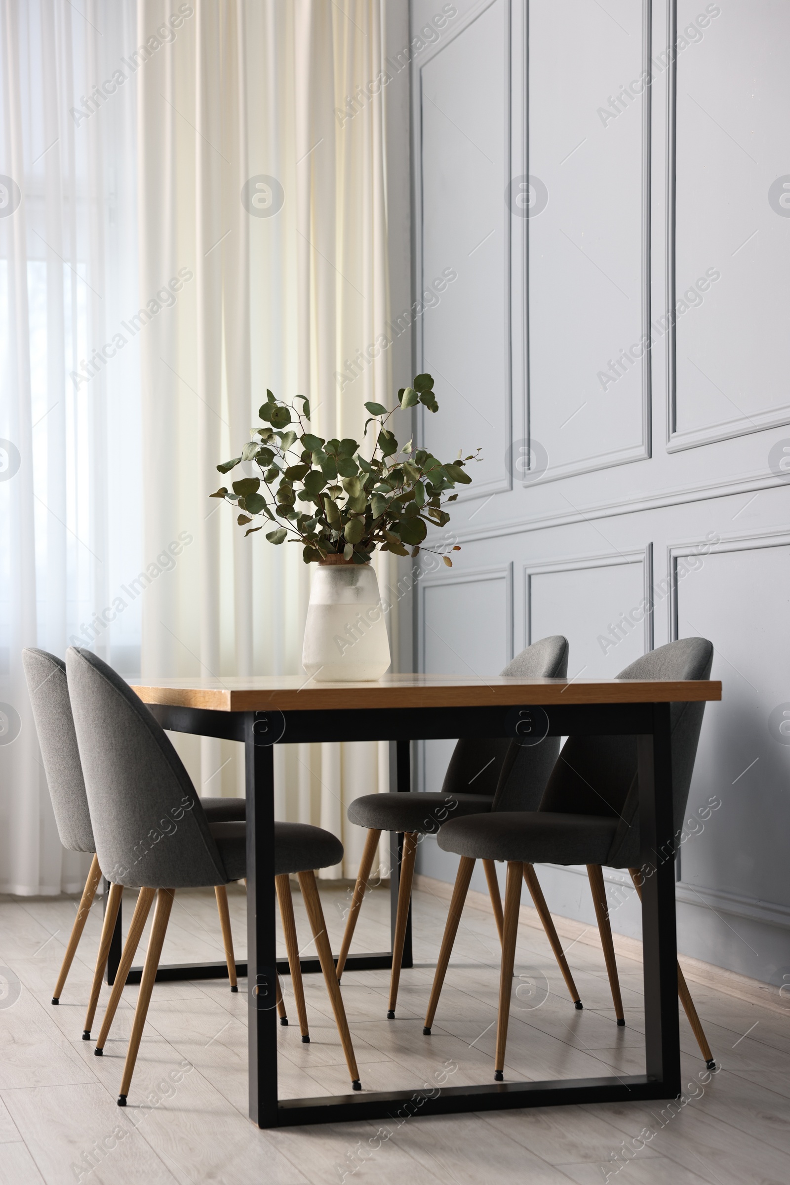 Photo of Soft chairs, table and vase with eucalyptus branches in stylish dining room