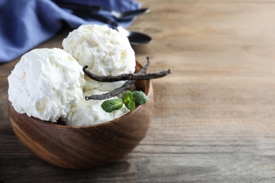 Photo of Yummy vanilla ice cream in bowl on wooden table. Space for text