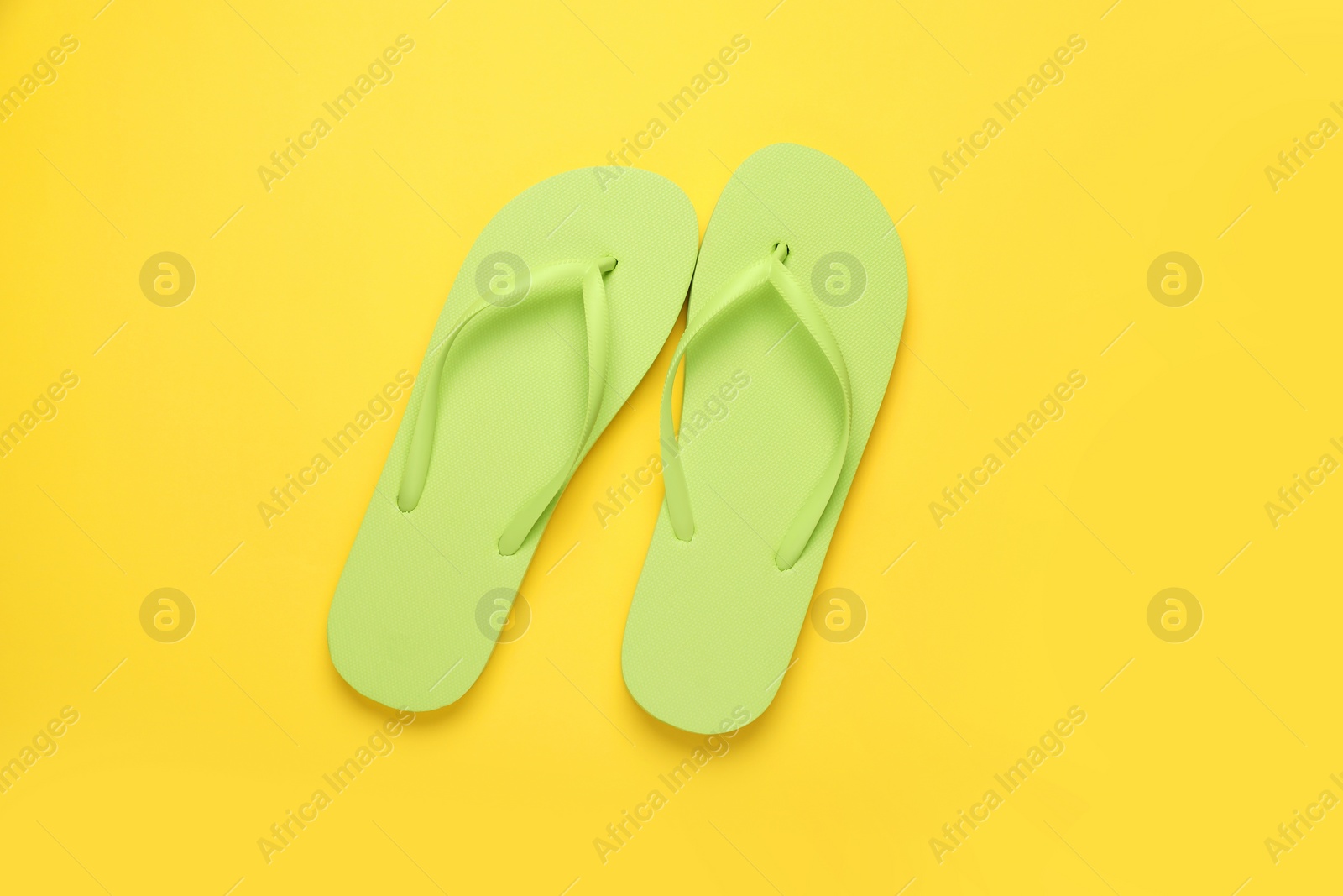 Photo of Stylish light green flip flops on yellow background, top view