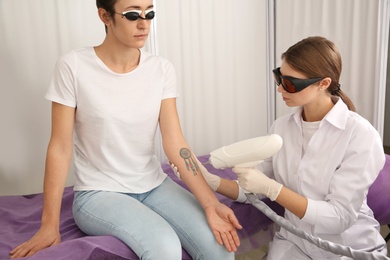 Photo of Young woman undergoing laser tattoo removal procedure in salon