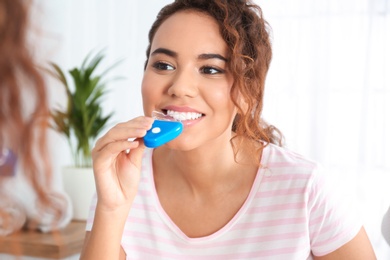 Young African-American woman using teeth whitening device at home