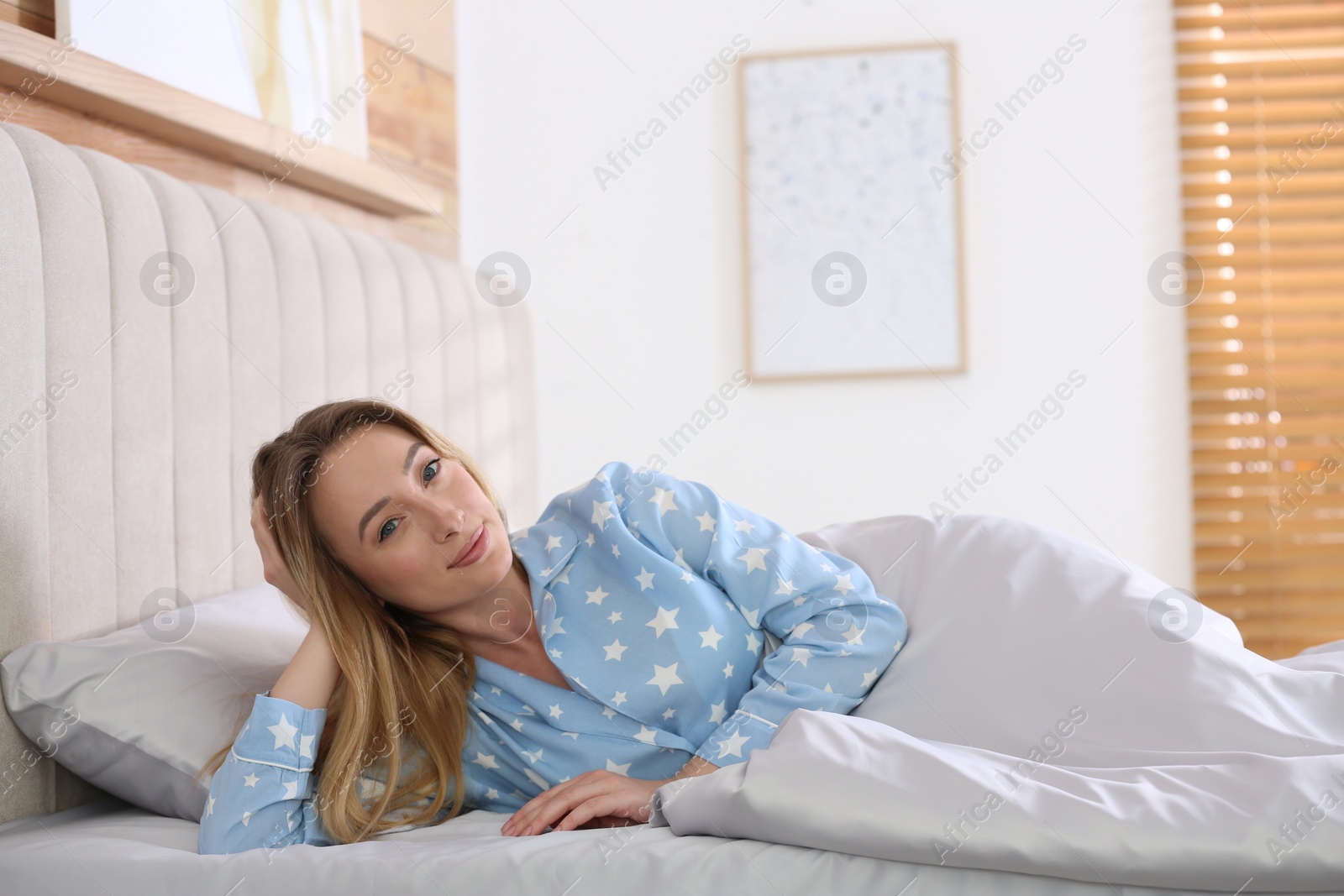 Photo of Young woman lying in comfortable bed with silky linens