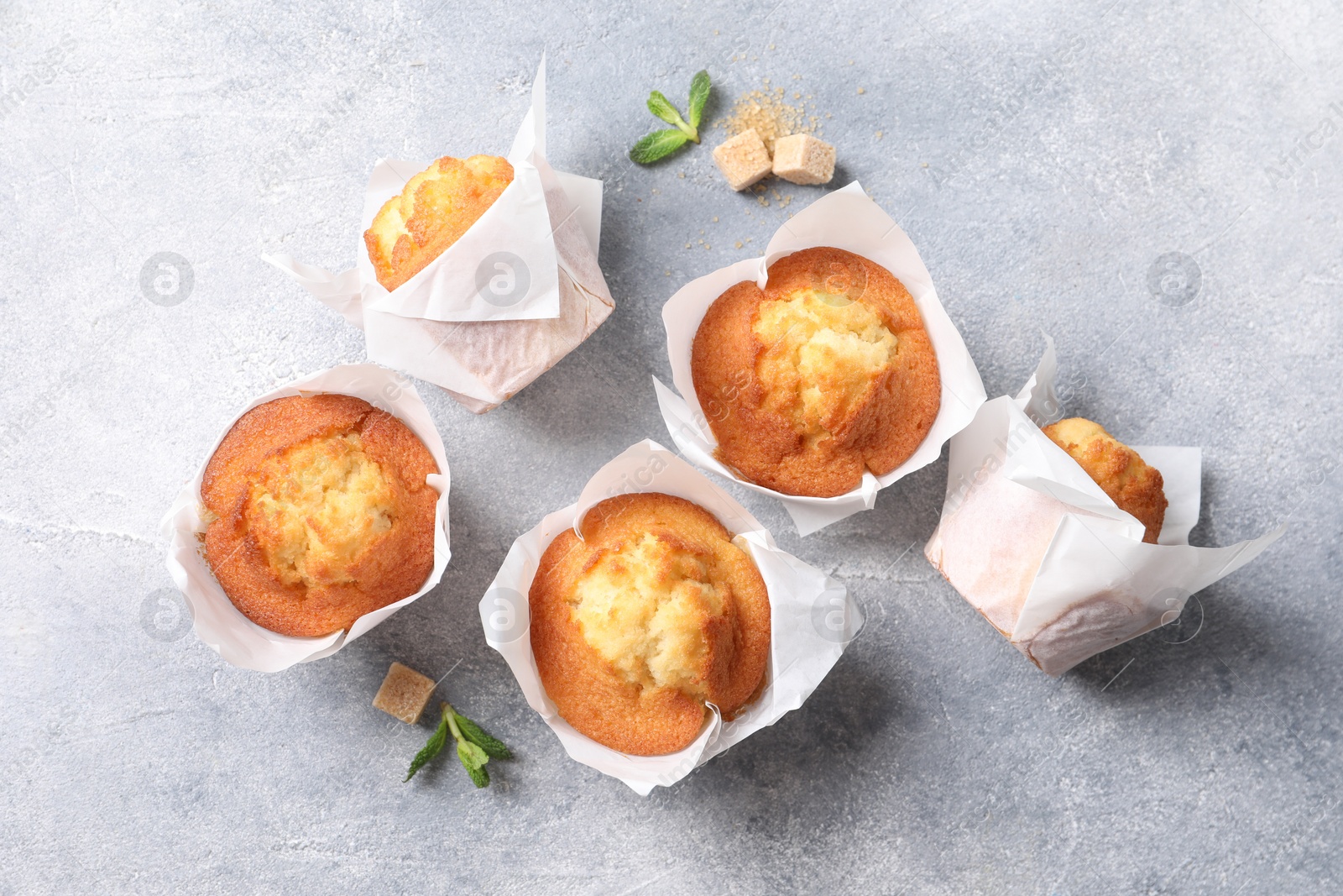 Photo of Delicious sweet muffins and brown sugar on light grey textured table, flat lay