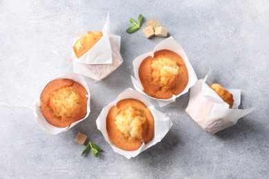 Delicious sweet muffins and brown sugar on light grey textured table, flat lay