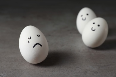 Photo of Egg with drawn sad face near happy ones on table. Threat of depression