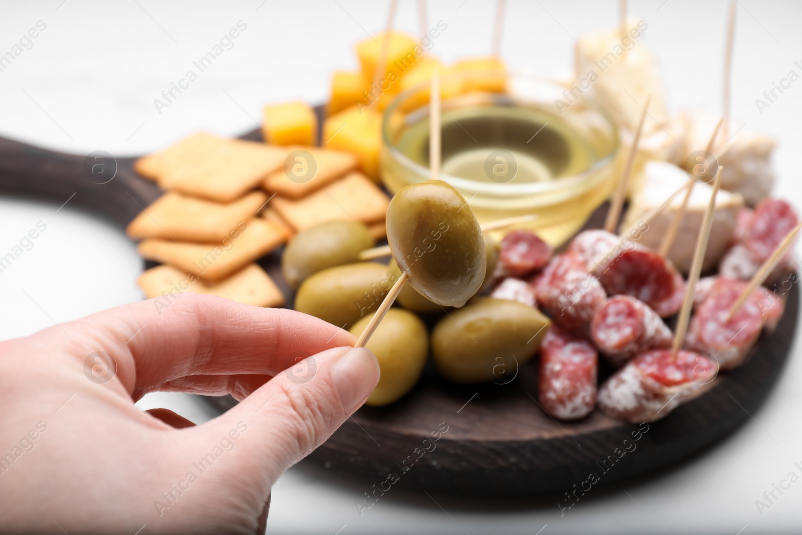 Photo of Woman holding toothpick with olive near white table, closeup