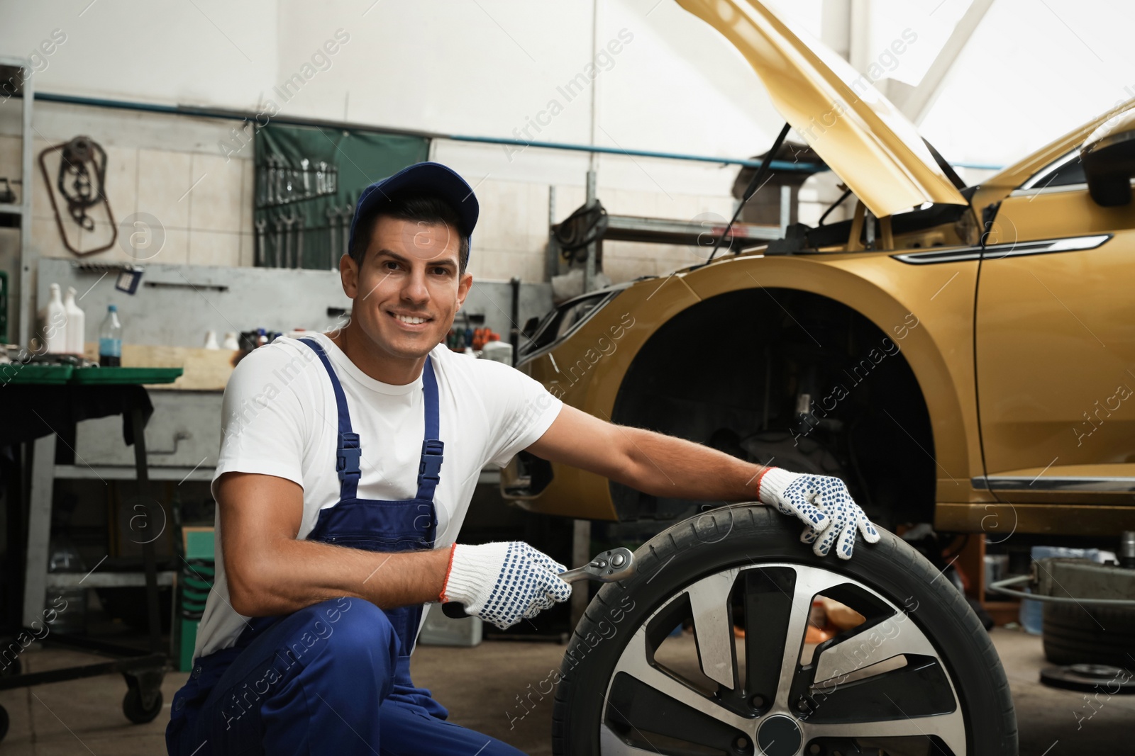 Photo of Portrait of professional mechanic with car wheel at automobile repair shop