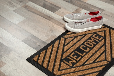 Photo of New clean doormat with word WELCOME and shoes on floor. Space for text