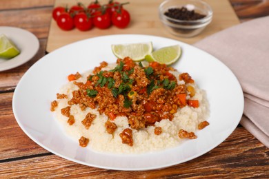 Photo of Tasty dish with fried minced meat, rice, carrot, corn and lime served on wooden table