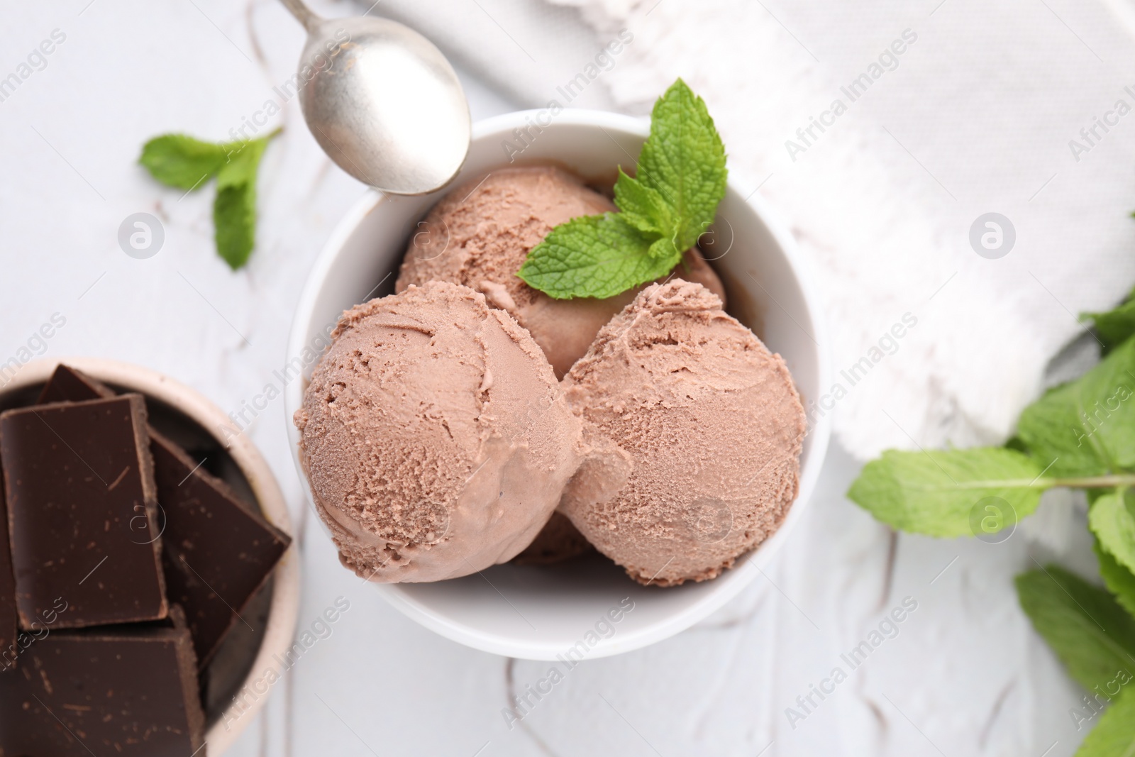 Photo of Bowl with tasty chocolate ice cream and mint leaves on white table, flat lay