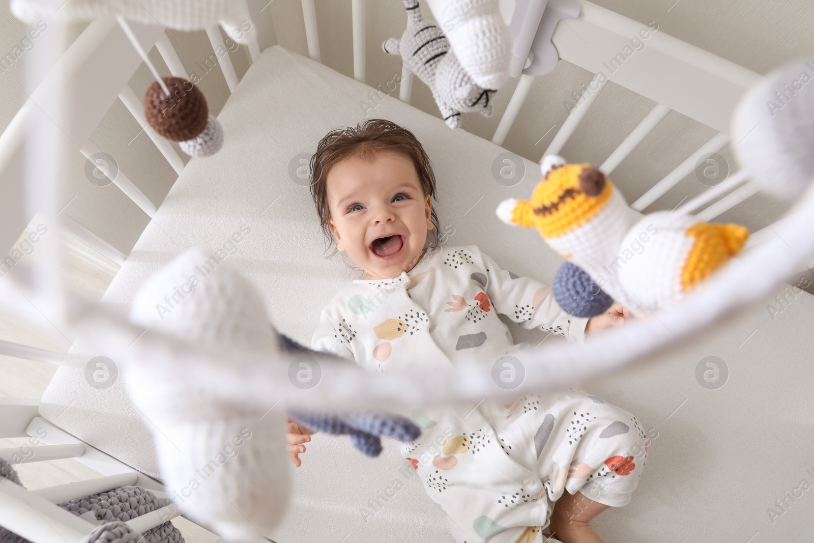 Photo of Cute little baby looking at hanging mobile in crib, top view