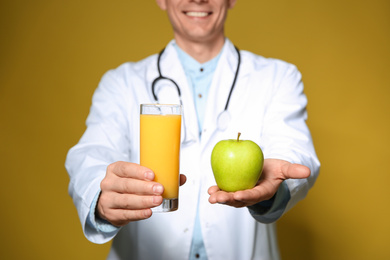 Photo of Nutritionist holding glass of juice and apple on yellow background, closeup