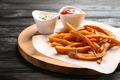 Board with sweet potato fries and sauces on wooden table