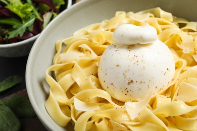Delicious pasta with burrata cheese in bowl on table, closeup