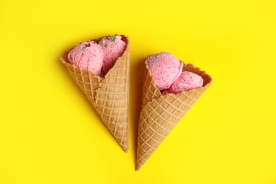 Photo of Delicious ice cream in wafer cones on yellow background, flat lay