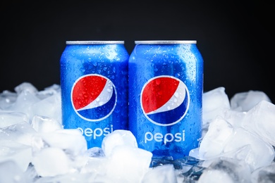 MYKOLAIV, UKRAINE - FEBRUARY 11, 2021: Cans of Pepsi on ice cubes against black background